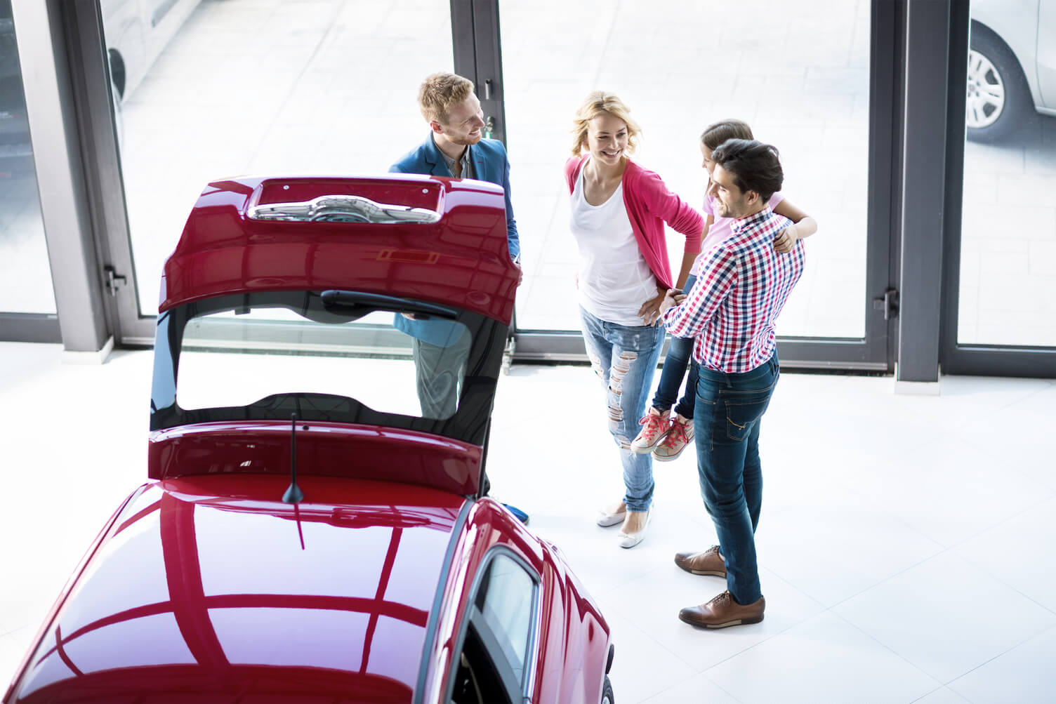 People looking at into the back of a car in a showroom floor.