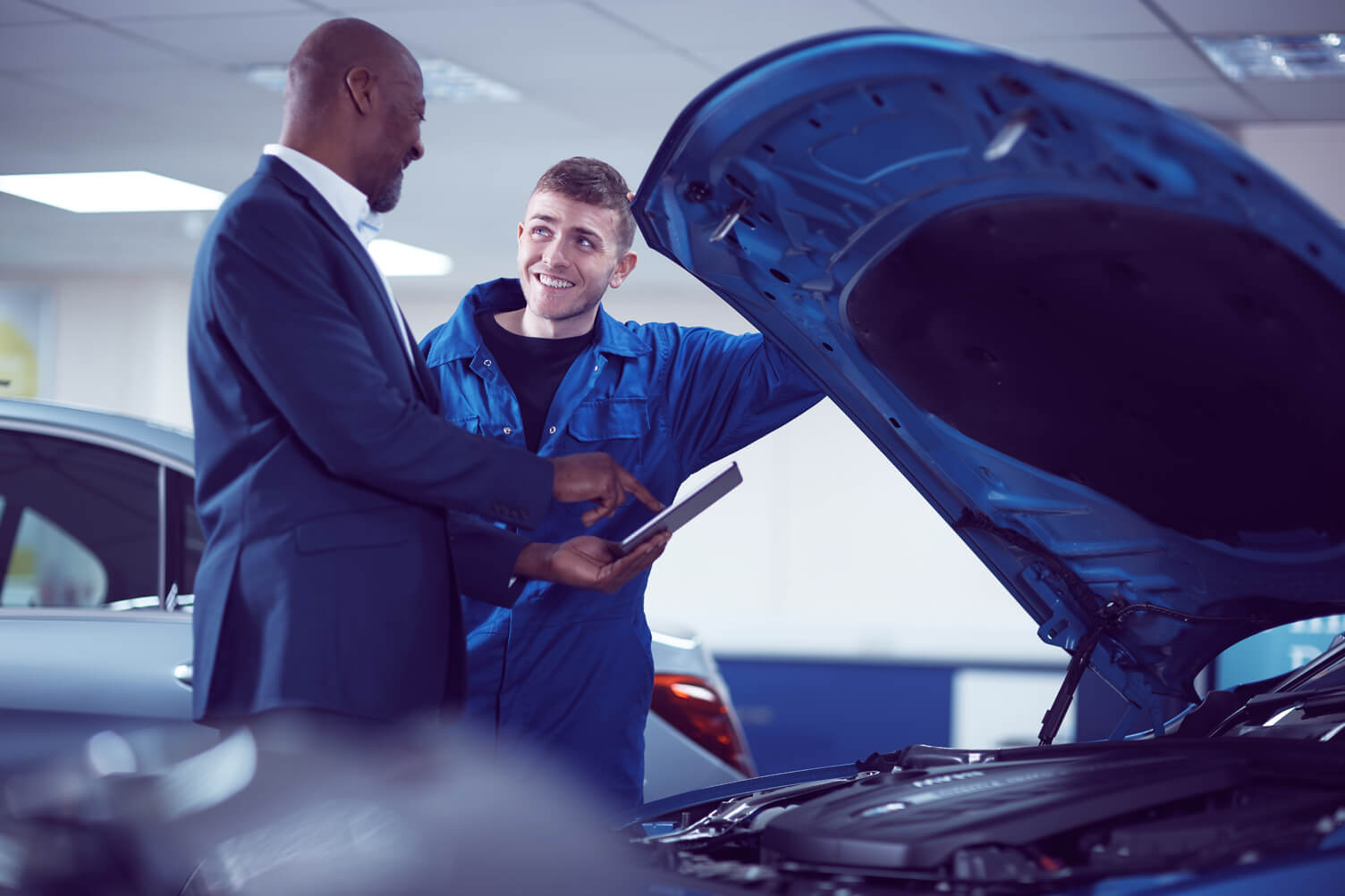 Customer and mechanic looking under the hood of a car.