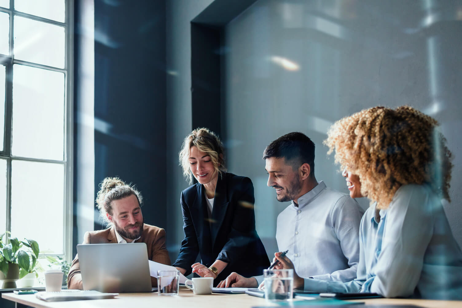 Multi ethnic team of four happy businessman and businesswoman discussing ideas together during a casual meeting at the office desk.