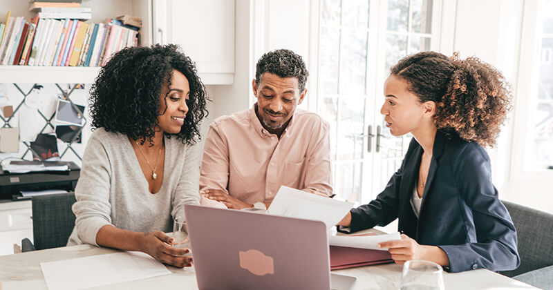 Three people sitting discussing paperwork at table